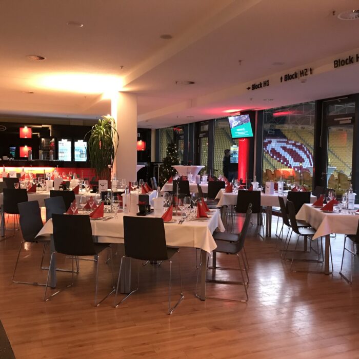 Veranstaltungsraum mit Tischen, Theke und Blick auf das Stadion.