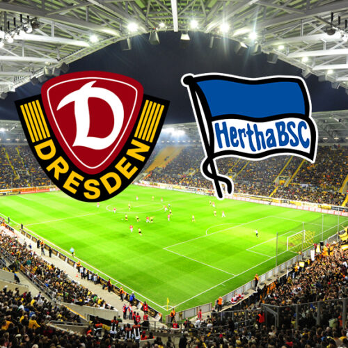 Ein breites, horizontales Bild zeigt ein Fußballstadion, das voll von Fans ist, die gelbe Trikots tragen. Auf dem Spielfeld sind Fußballspieler zu sehen. Am oberen Rand des Bildes, in der Mitte, befinden sich zwei Logos. Das linke Logo ist das Wappen von Dynamo Dresden, das rechte Logo ist das Wappen von Hertha BSC.