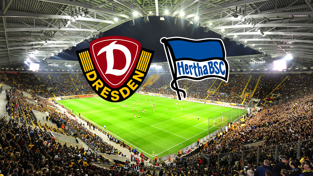 Ein breites, horizontales Bild zeigt ein Fußballstadion, das voll von Fans ist, die gelbe Trikots tragen. Auf dem Spielfeld sind Fußballspieler zu sehen. Am oberen Rand des Bildes, in der Mitte, befinden sich zwei Logos. Das linke Logo ist das Wappen von Dynamo Dresden, das rechte Logo ist das Wappen von Hertha BSC.